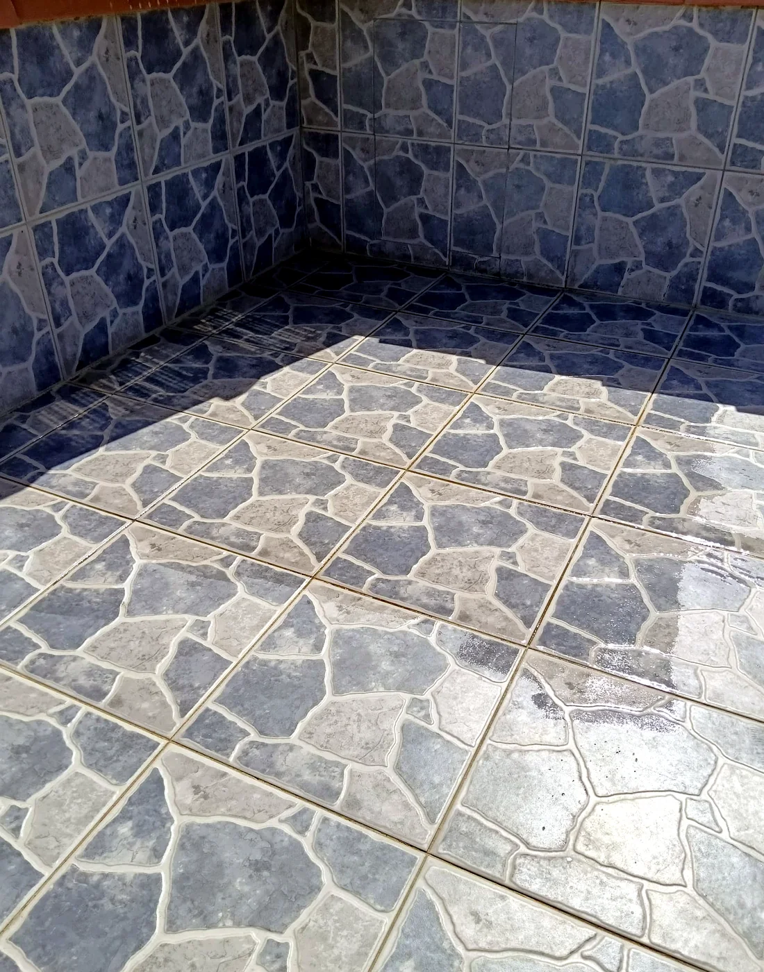 Stone-pattern ceramic floor and wall tiles meeting at a neatly grouted corner