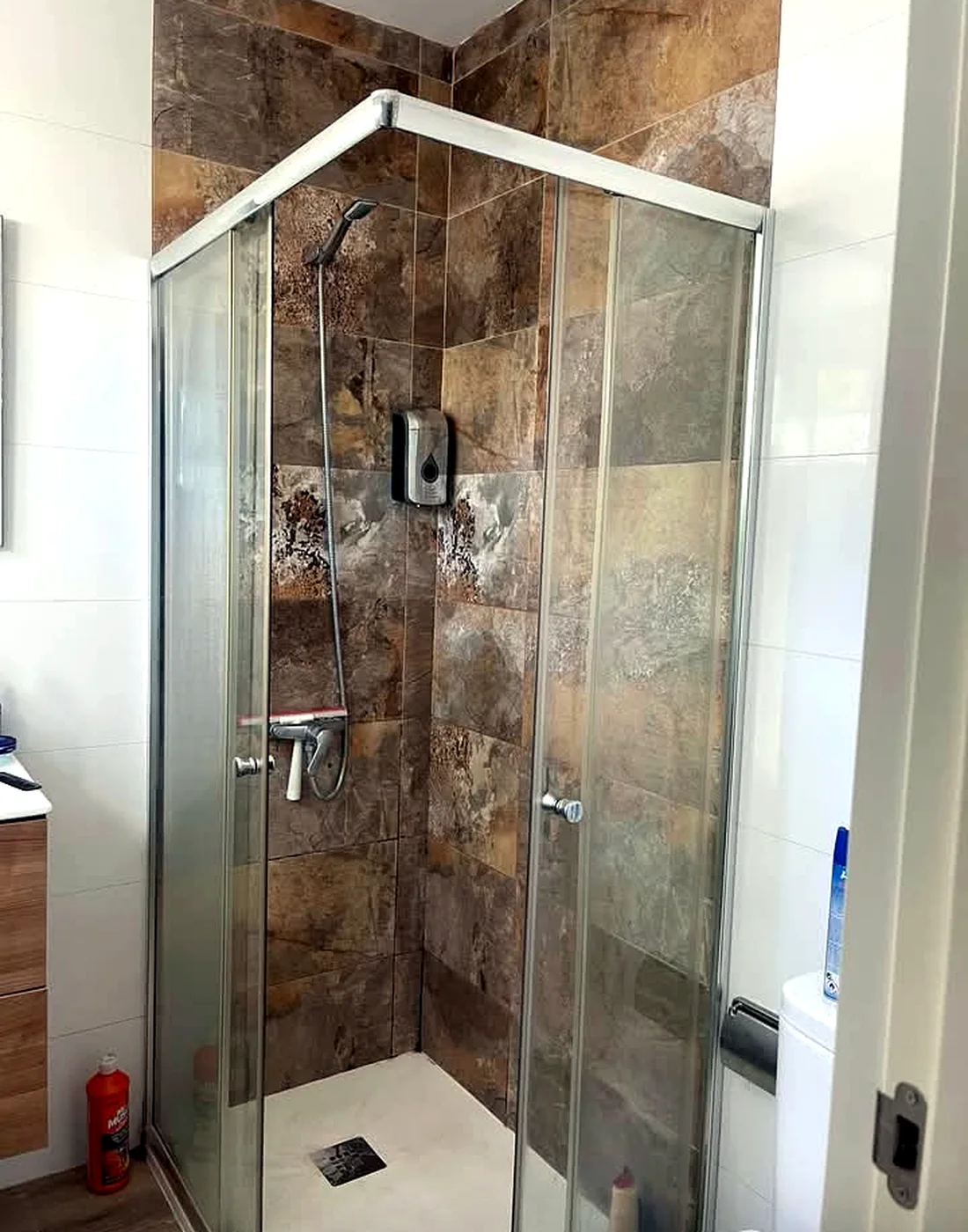 Glass shower enclosure with stone-pattern wall tiles and white shower tray