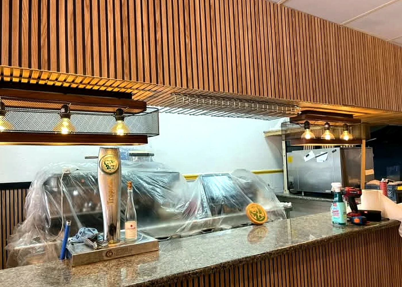 Detail of timber-slat bar canopy, suspended lights and countertop during installation