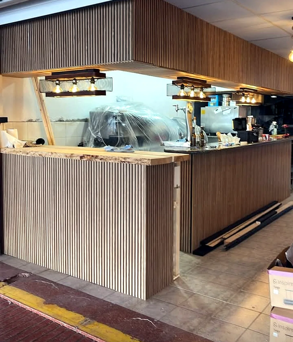 Bar joinery with vertical timber slats on the counter front and overhead canopy during installation