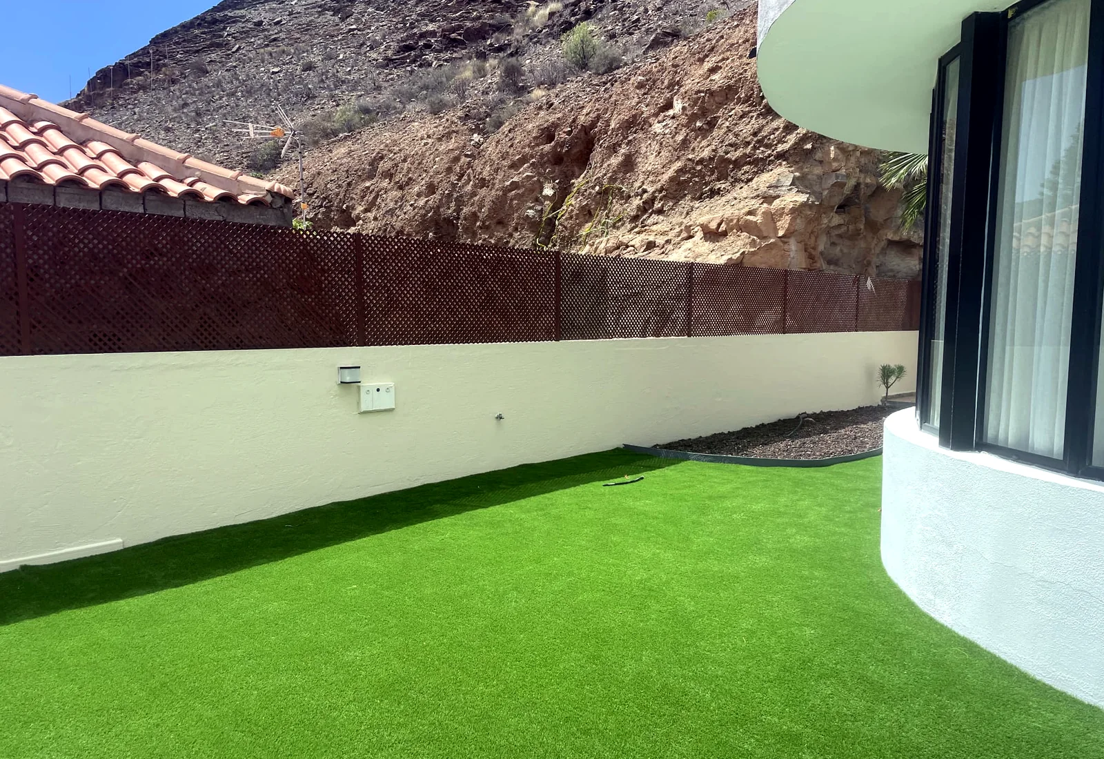 Exterior garden with artificial grass, rendered boundary wall and curved glazed building frontage